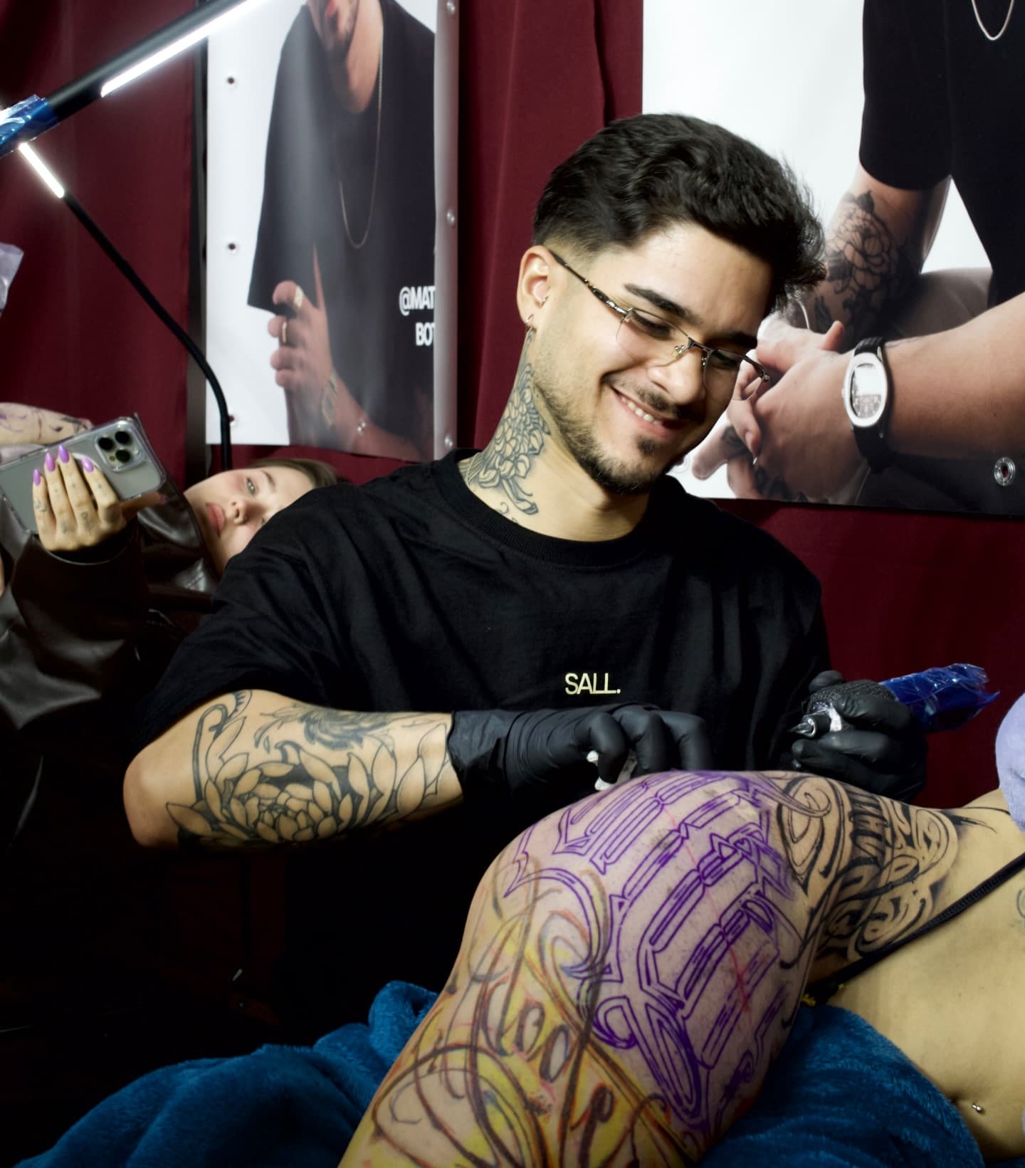 Théo Farias a tatuar um lettering na perna de um cliente, concentrado e a sorrir