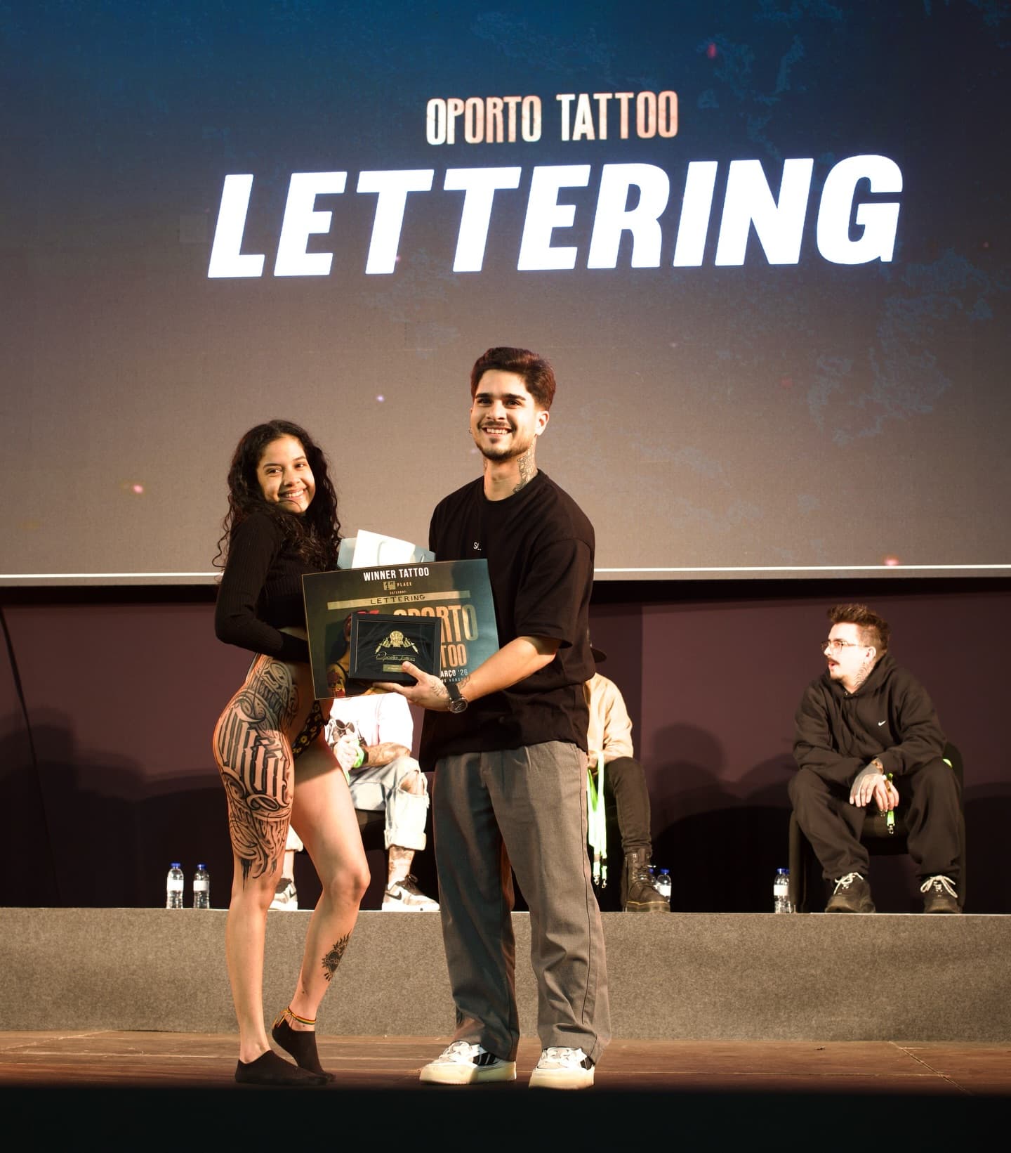 Théo Farias e cliente no palco da Oporto Tattoo, a segurar o prémio de 1º lugar em Lettering