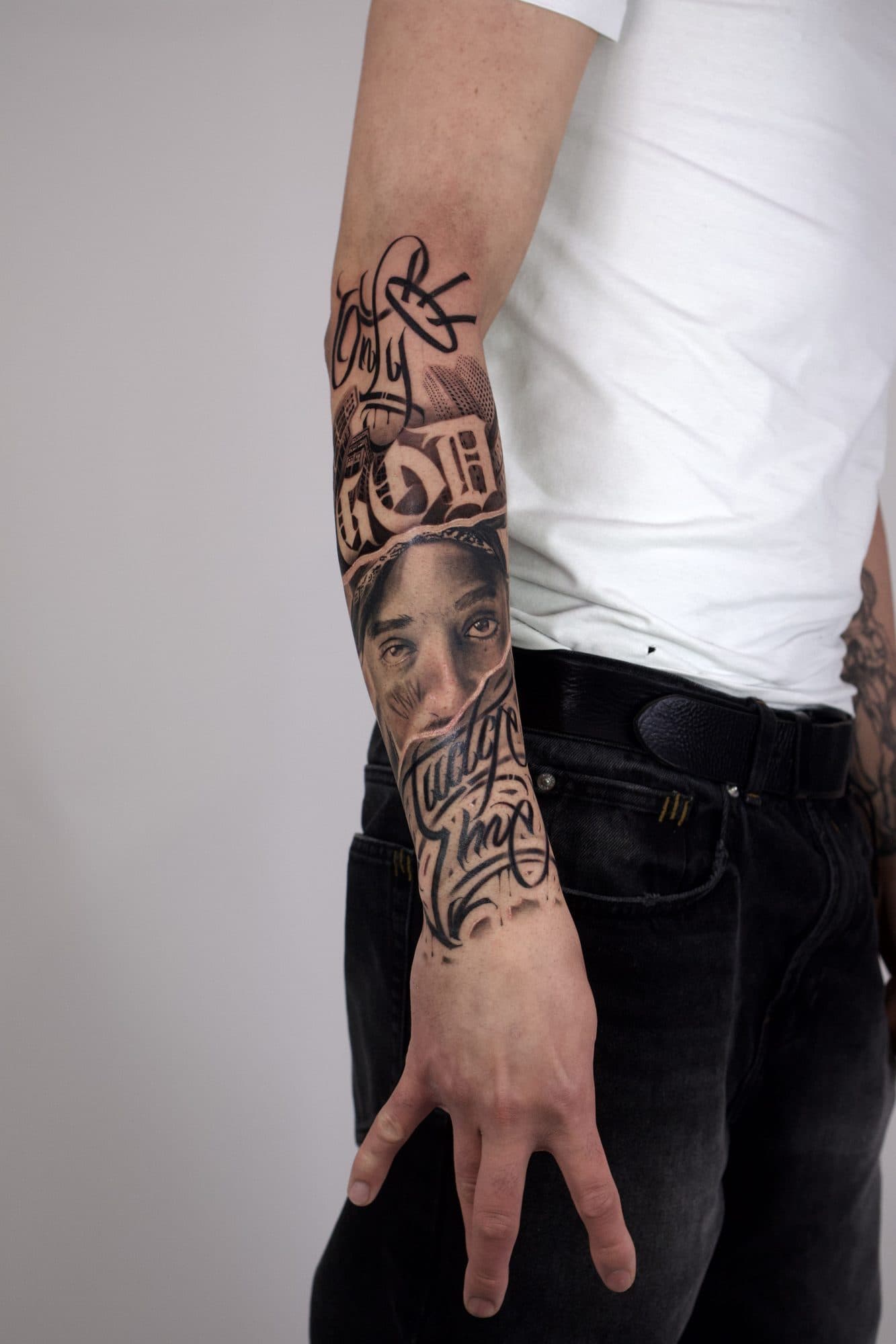 Manga em black and grey no antebraço, com lettering e retrato realista de rosto com bandana