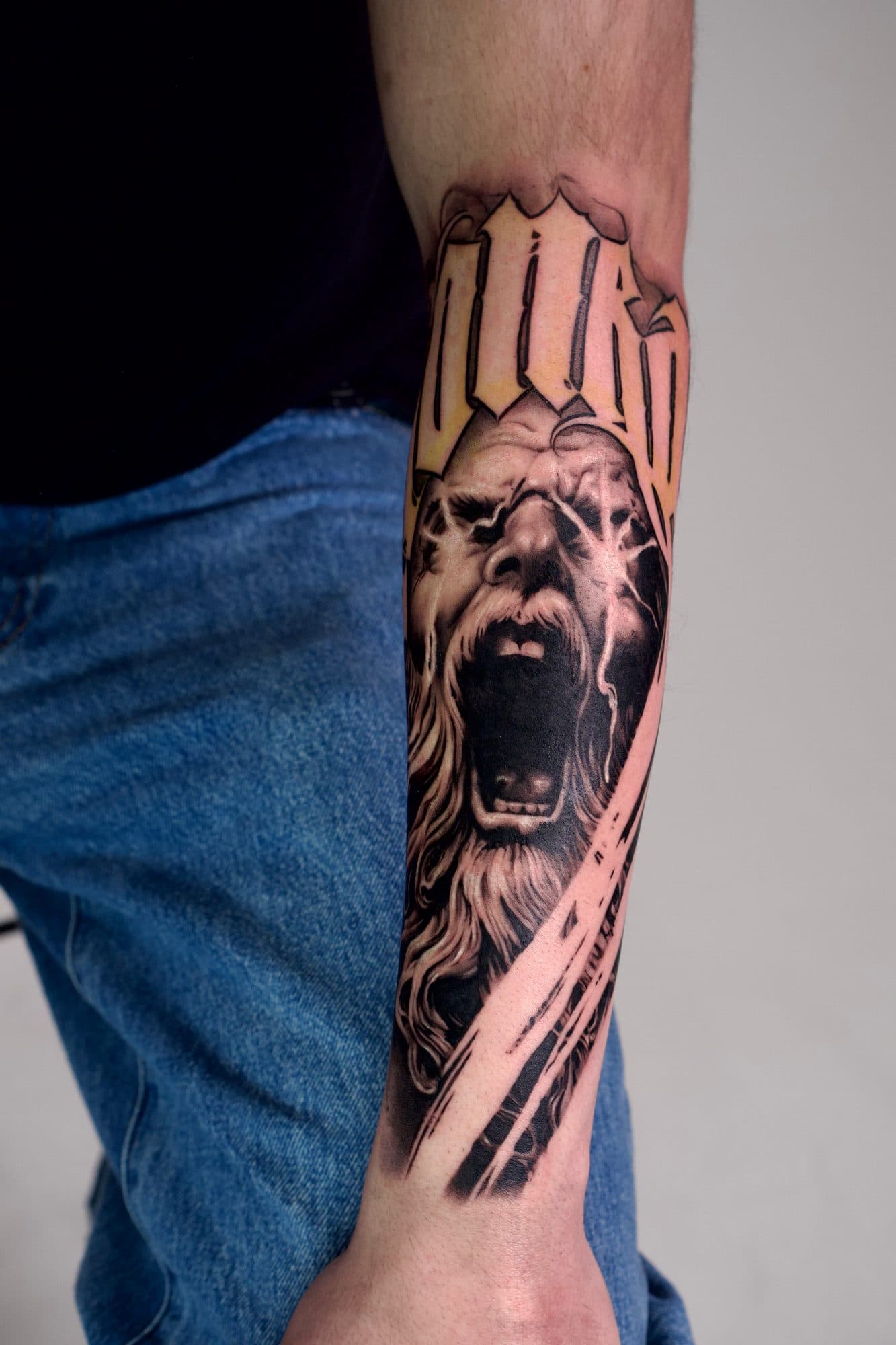 Antebraço em black and grey com rosto de fera a rugir sob lettering