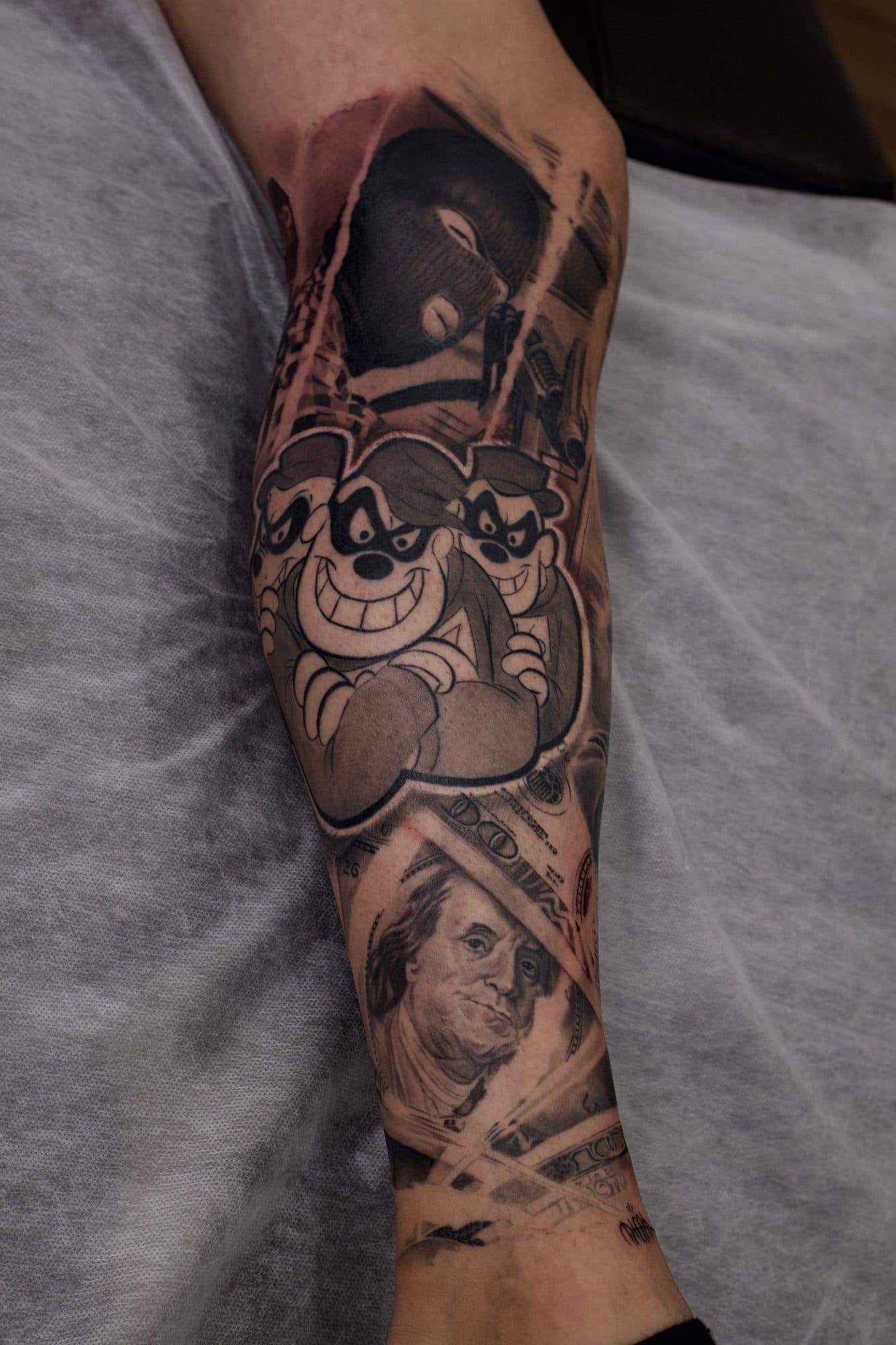 Antebraço em black and grey com personagens de desenho animado e nota de dólar