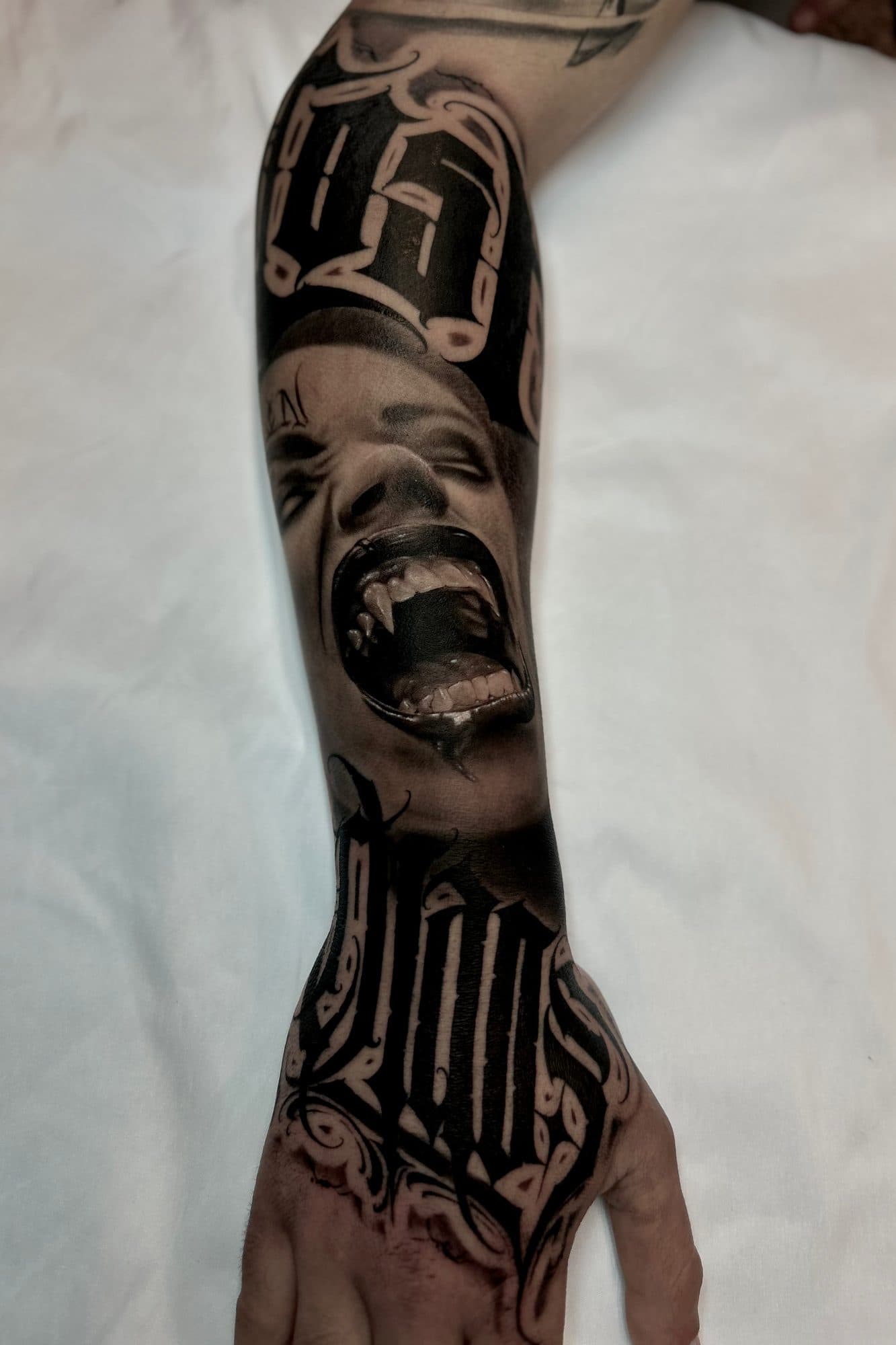 Braço em black and grey com rosto a gritar entre lettering em blackletter