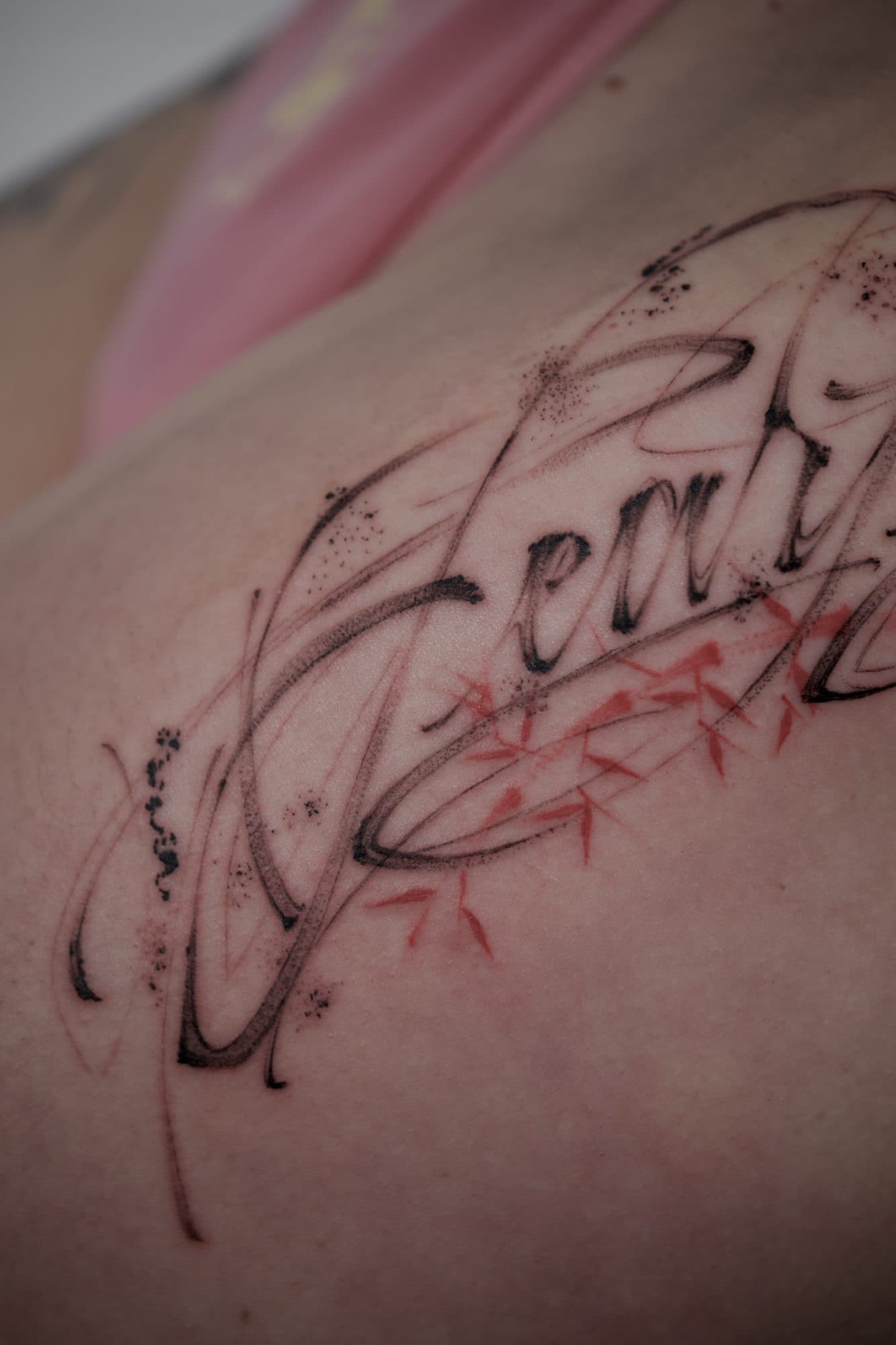Lettering pincelado nas costas, em traço solto de pincel a preto com detalhes a vermelho
