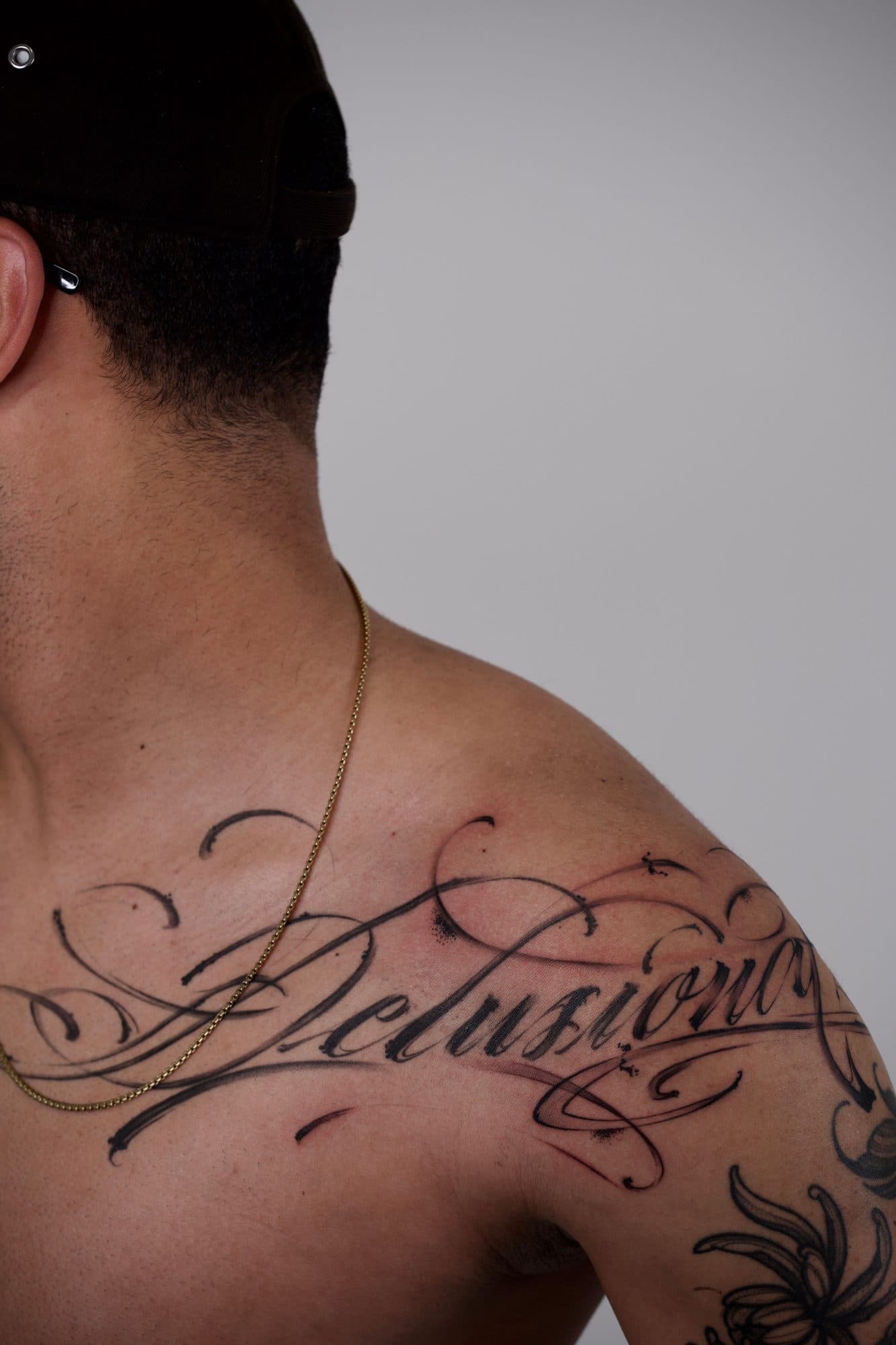 Lettering pincelado «Delusions» na clavícula e ombro