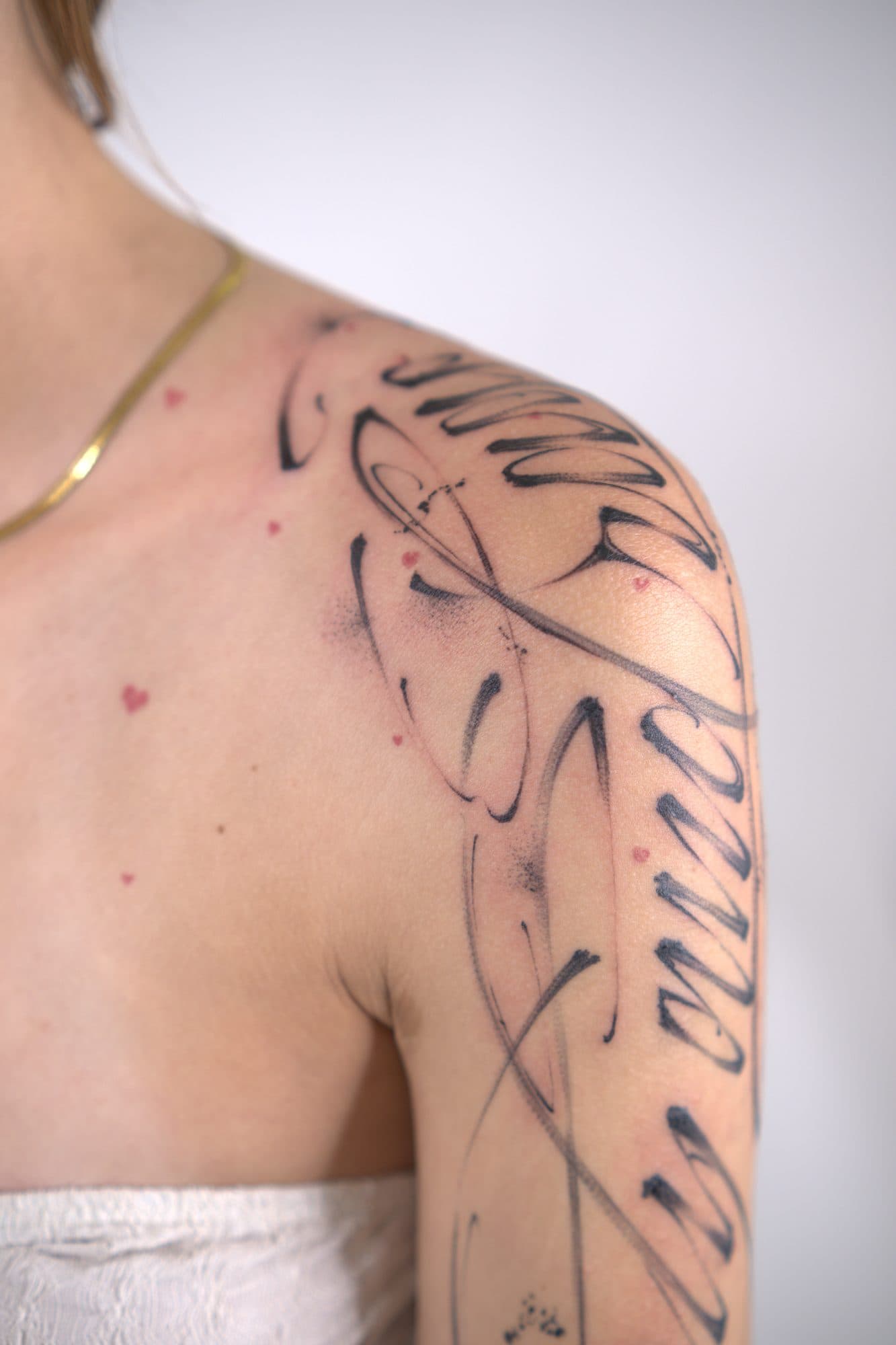 Lettering pincelado em traço fino a descer pelo ombro e braço