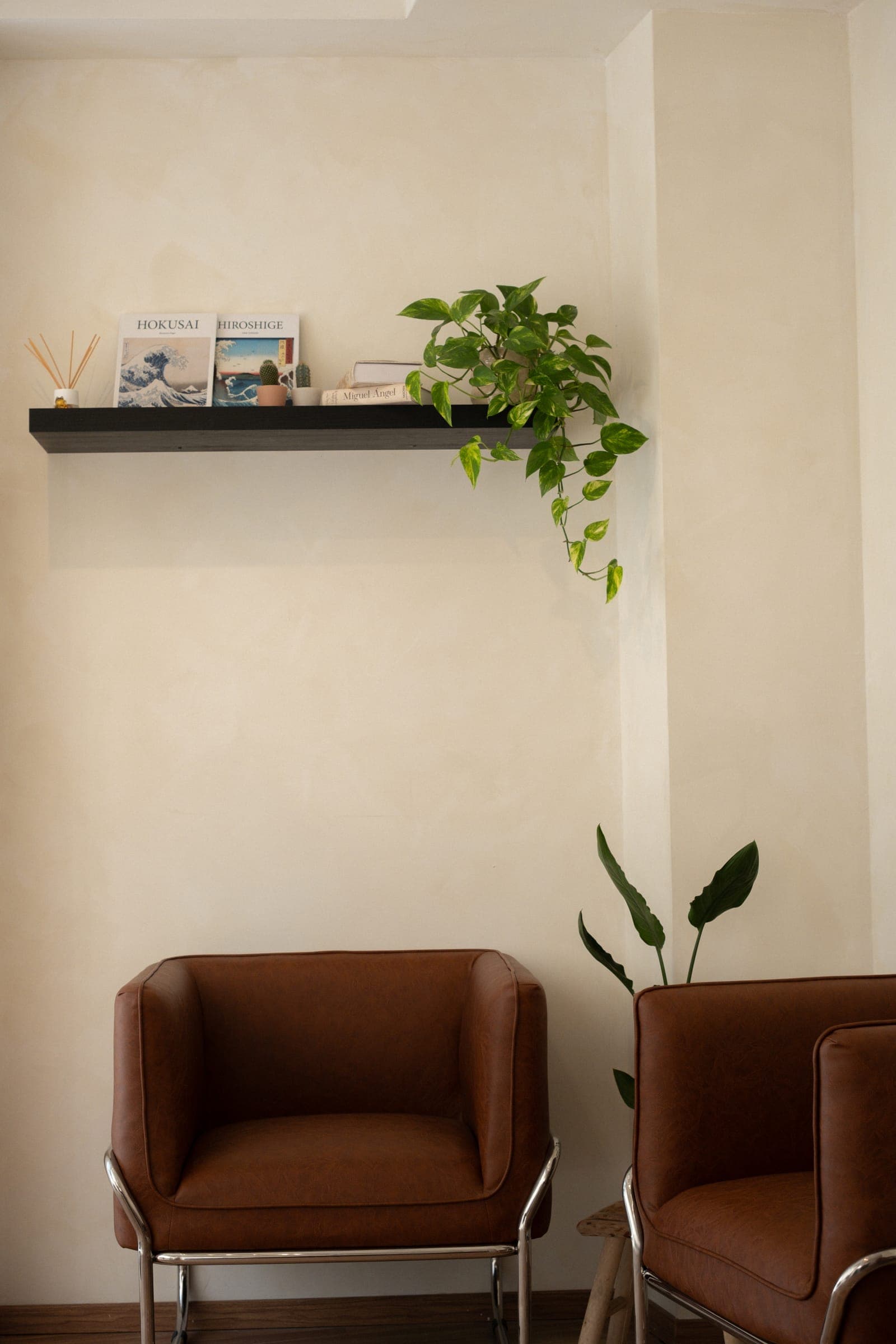 Zona de espera com poltronas de couro castanho, plantas e livros de Hokusai e Hiroshige na prateleira