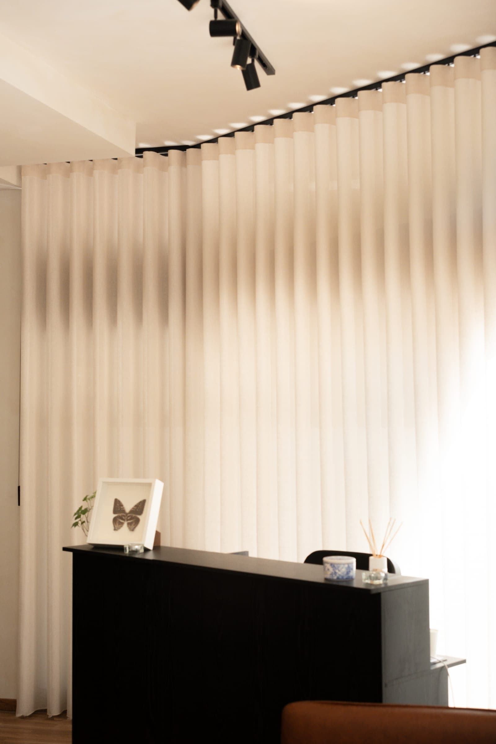Receção com balcão preto, quadro de borboleta e cortina de linho iluminada pela luz natural